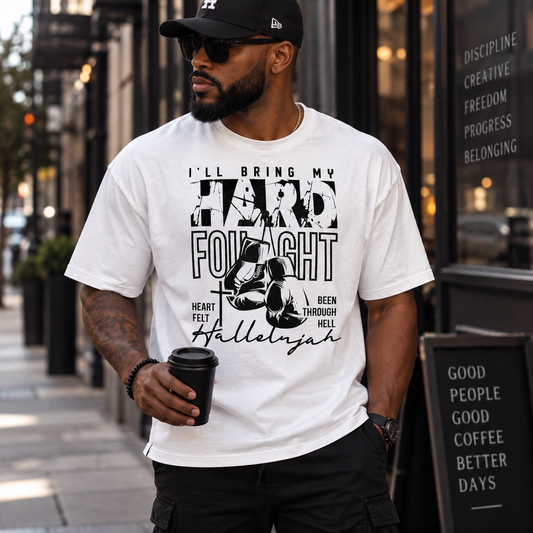 A man wearing a white graphic t-shirt with a black print that reads 'I'LL BRING MY HARD FOILIGHT' and 'Hallelujah' with a halftone graphic, standing on a city street.