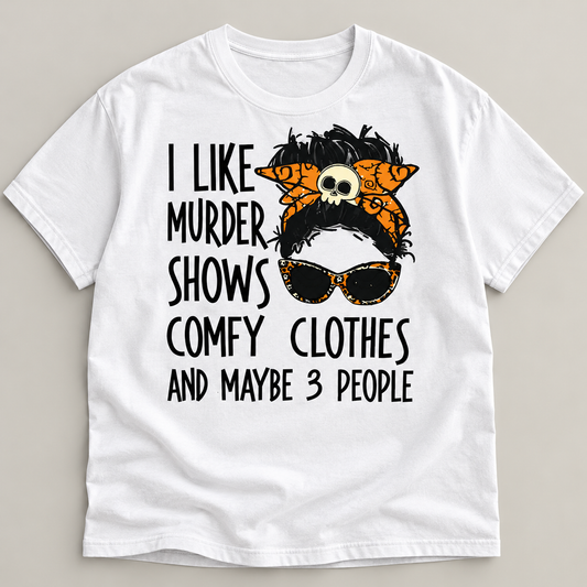 A white short-sleeve crewneck t-shirt with a graphic print on the front. The graphic features a stylized portrait of a woman with black hair, an orange and black patterned headscarf with a skull detail, and black sunglasses.
