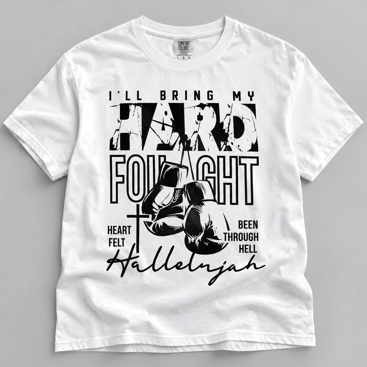 A white short-sleeve crewneck t-shirt with a black graphic print on the front. The graphic features the text 'I'LL BRING MY HARD FOUGHT' with boxing gloves, a cross, and the name 'Hallelnjah' written in script.
