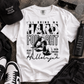 A white graphic t-shirt laid flat on a textured gray surface, surrounded by lifestyle props including a black baseball cap, sunglasses, a water bottle, sneakers, and black jeans. The t-shirt features a distressed black graphic of boxing gloves and the text 'I'LL BRING MY HARD FOILIGHT' and 'Hallelujah'.