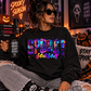 A woman wearing a black sweatshirt with a colorful 'SPOOKY season' graphic sits in a cozy, Halloween-themed room. She holds a black mug with the text 'GOOD MOVIES SCARY PEOPLE' and wears ripped gray jeans.