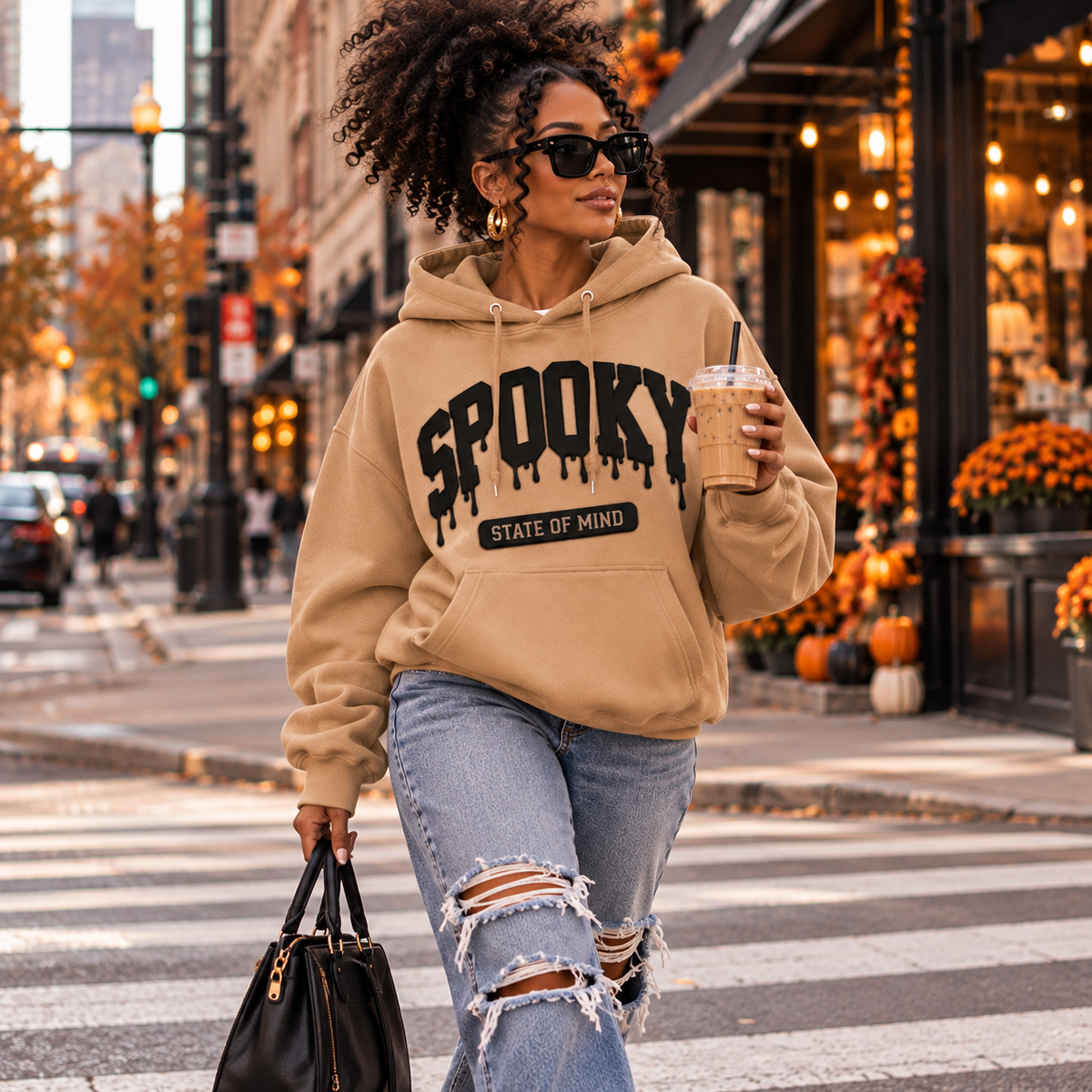 Black woman with curly puff hair wearing a Meerkat Spooky State of Mind puff vinyl hoodie while crossing a downtown street