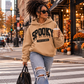 Black woman with curly puff hair wearing a Meerkat Spooky State of Mind puff vinyl hoodie while crossing a downtown street