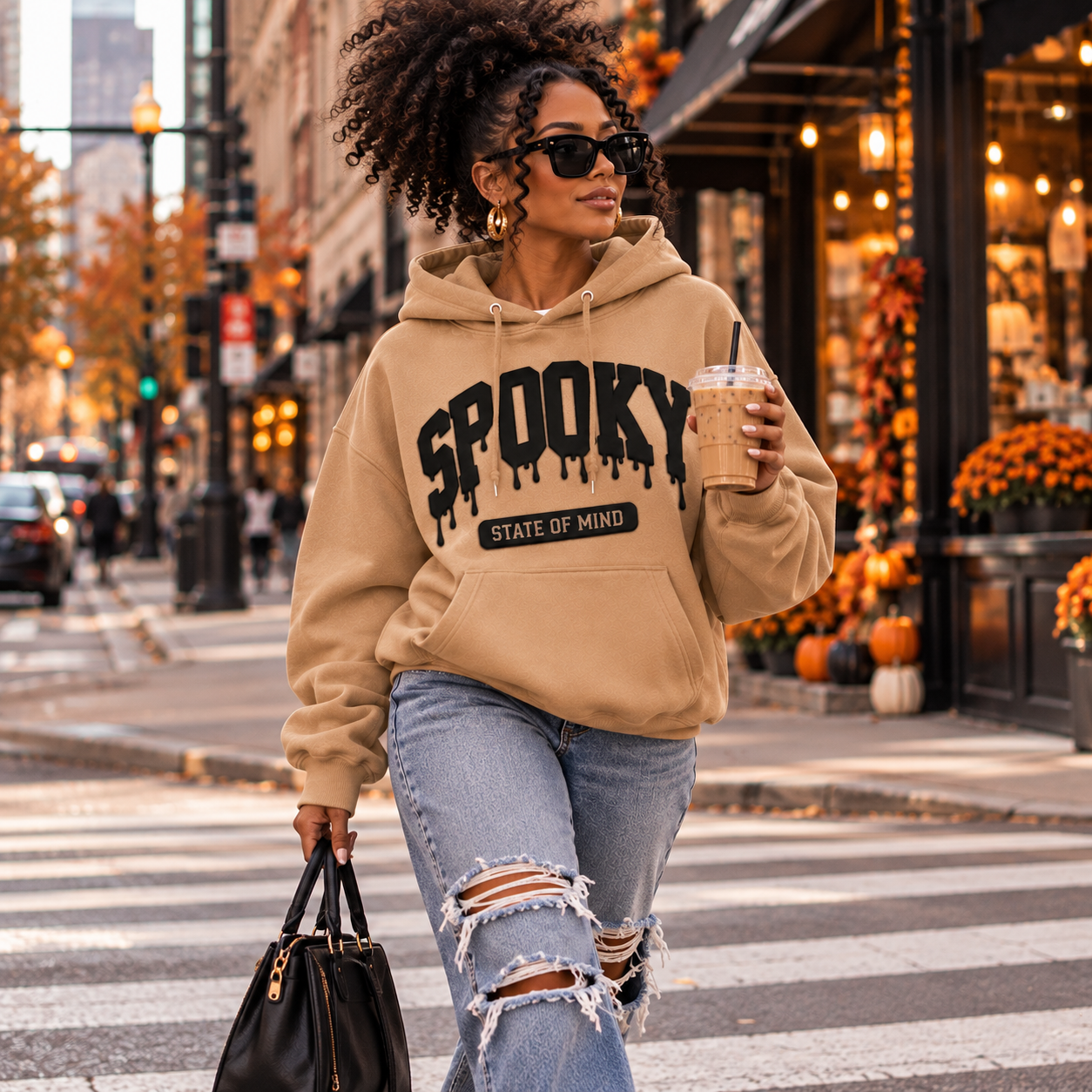 Black woman with curly puff hair wearing a Meerkat Spooky State of Mind puff vinyl hoodie while crossing a downtown street