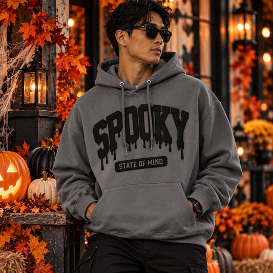 Male model wearing a Storm gray Spooky State of Mind hoodie with raised black puff vinyl lettering in an autumn Halloween setting